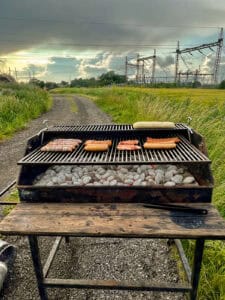 Grill med mad i forgrunden og et åbent landskab med elmaster i baggrunden.