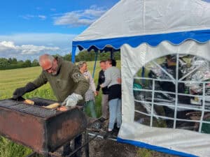 Mand griller mad ved grill, mens andre snakker uden for teltet.