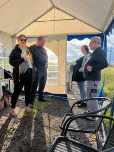 Fire personer i uformel samtale i telt under sollys.