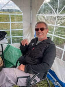 Smilende mand sidder afslappet i telt med grøn mark synlig bag vinduerne.